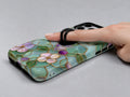 Aqua Grape Stained Glass Floral MagSafe Loop iPhone Case shown in use with a finger through the horizontal loop
