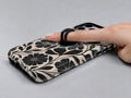 Black Cream Bold Floral MagSafe Loop iPhone Case shown in use with a finger through the horizontal loop