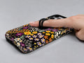Black Folk Garden Floral MagSafe Loop iPhone Case shown in use with a finger through the horizontal loop