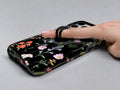 Black Wildflower Meadow MagSafe Loop iPhone Case shown in use with a finger through the horizontal loop