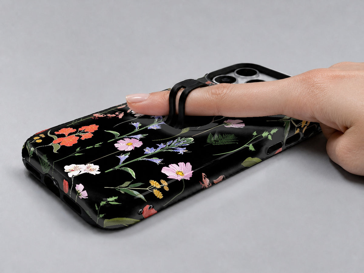 Black Wildflower Meadow MagSafe Loop iPhone Case shown in use with a finger through the horizontal loop