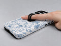 Blue Toile Wildflower MagSafe Loop iPhone Case shown in use with a finger through the horizontal loop