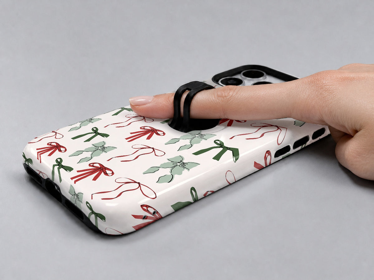 Christmas Bow and Mistletoe MagSafe Loop iPhone Case shown in use with a finger through the horizontal loop