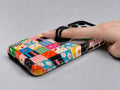 Colorful Folk Quilt Patchwork MagSafe Loop iPhone Case shown in use with a finger through the horizontal loop