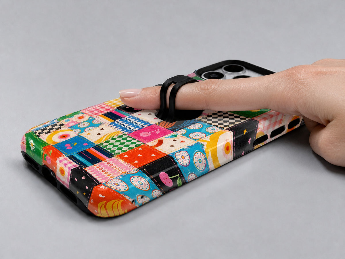 Colorful Folk Quilt Patchwork MagSafe Loop iPhone Case shown in use with a finger through the horizontal loop