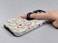 Colorful Pressed Wildflower MagSafe Loop iPhone Case shown in use with a finger through the horizontal loop