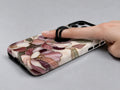 Dusty Rose Magnolia Floral MagSafe Loop iPhone Case shown in use with a finger through the horizontal loop