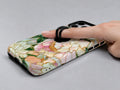 Green Peach Stained Glass Floral MagSafe Loop iPhone Case shown in use with a finger through the horizontal loop