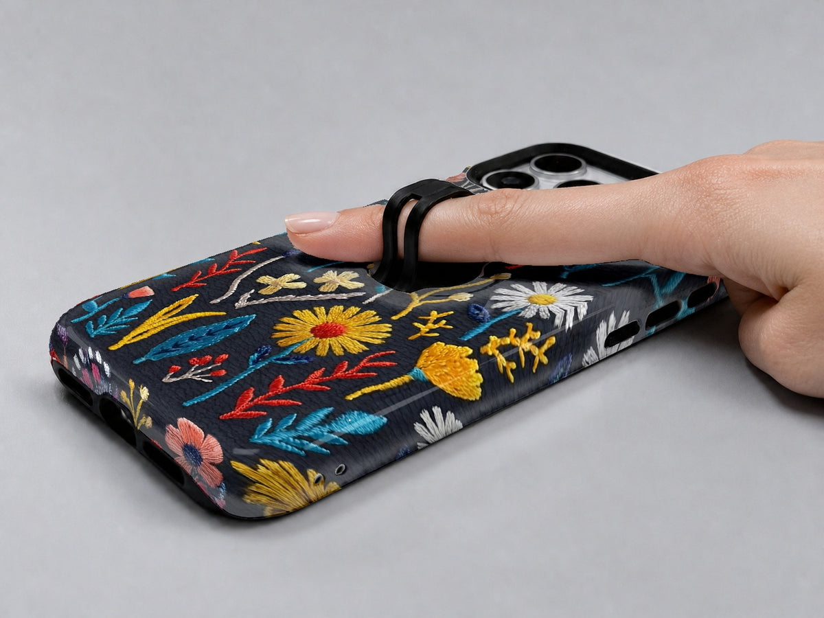Navy Embroidered Wildflower MagSafe Loop iPhone Case shown in use with a finger through the horizontal loop