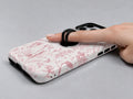 Pink Toile Wildflower MagSafe Loop iPhone Case shown in use with a finger through the horizontal loop