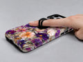 Purple Wildflower Glass Garden MagSafe Loop iPhone Case shown in use with a finger through the horizontal loop