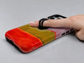 Rose Olive Scarlet Color Block MagSafe Loop iPhone Case shown in use with a finger through the horizontal loop