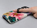Teal Pink Stained Glass Floral MagSafe Loop iPhone Case shown in use with a finger through the horizontal loop